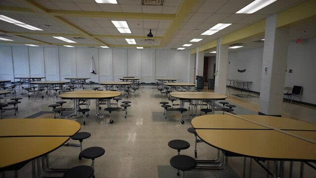 Trucking view to left showing empty school cafeteria with tables and seats.
