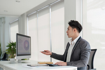 Fototapeta premium Handsome smiling businessman sitting in office and working on laptop screen