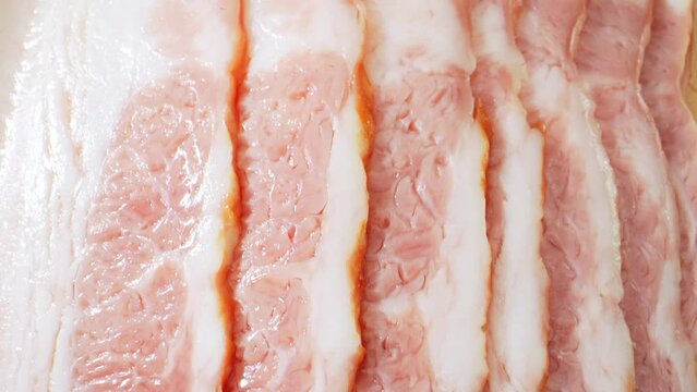 A tantalizing exploration of raw bacon through a macro lens. Experience the intricate layers of fat and meat, unveiling the essence of this savory delight. Food concept. Bacon background. 4K
