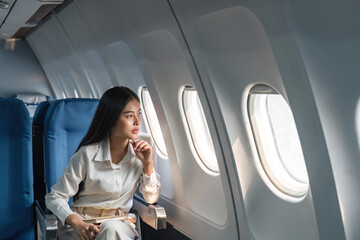 Asian woman passenger sitting in airplane near window and looking out the window