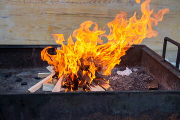 Obraz premium flames with smoke from burning firewood on an iron pallet of a barbecue with coals. Cooking coals for barbecue