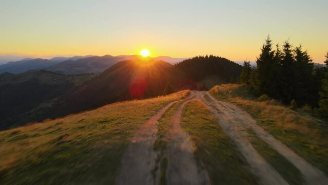 Offroad path crossing hill top. Dark dirt road illuminated with bright setting sun. Amazing sunset scenery in wild mountain forest. Beautiful nature landscape