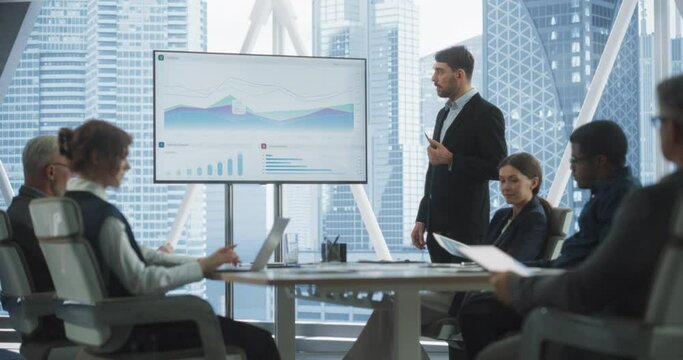 Office Conference Room Meeting Presentation: Caucasian CEO Talks, Uses TV to Show Company Growth with Big Data Analysis, Graphs, Charts, Infographics. Multi-Ethnic e-Commerce Startup Workers.