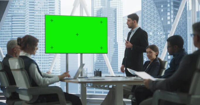 Office Conference Room Meeting Presentation: Caucasian Businessman Talks, Uses Green Screen Chroma Key TV Set. Male CEO Successfully Presenting a e-Commerce Product to Group of Multi-Ethnic Investors.
