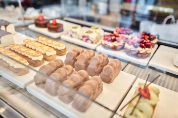 A variety of cakes covered with chocolate and decorated with pistachio mousse. A showcase in a pastry shop with delicious desserts with fresh berries and cream. Delicious pastries in the coffee shop.