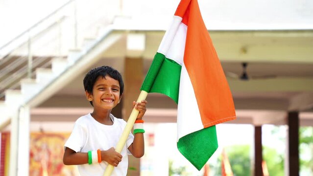 Cute little boy holding Indian flag in his hands and smiling. Celebrating Independence day or Republic day in India. Kid showing pride of Tiranga