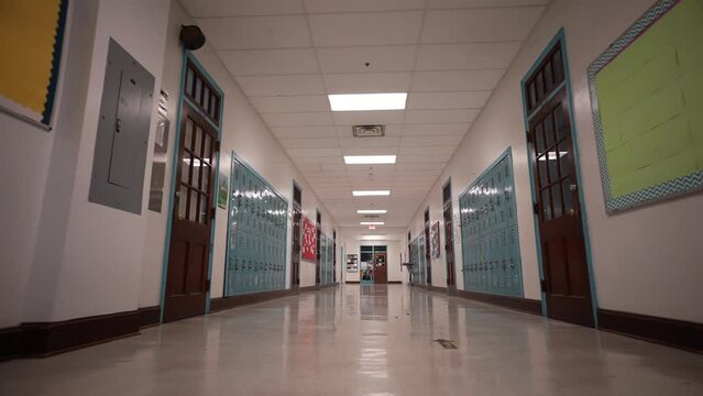 Low angle push in down a long empty high school corridor hallway lined with student lockers.
