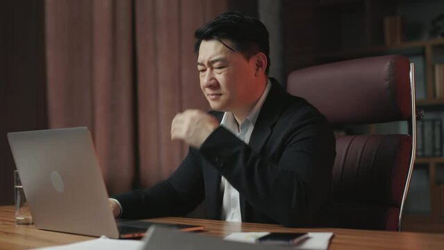 Angle view of annoyed asian man wearing formal outfit having problems with data loss at office workplace. Confused gentleman feeling stress, touching head and closing computer.