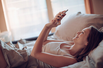 Young woman using a smart phone in the bed in the bedroom