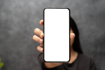 Mock up of beautiful woman pointing finger at mobile phone with blank white screen. Close up image of Asian woman showing blank screen mobile phone