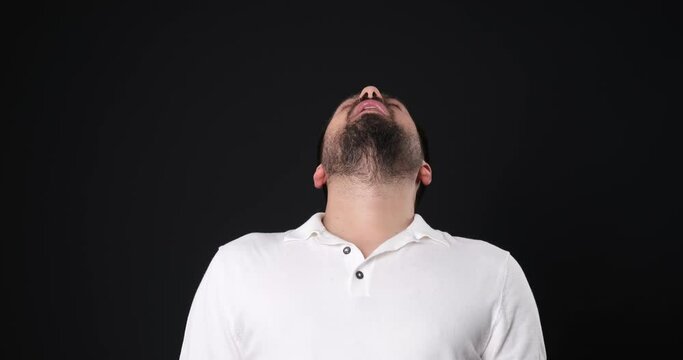 The when a middle-aged man in a studio setting, through close-up shots, looks at the camera and makes gestures and facial expressions that indicate being sleepy