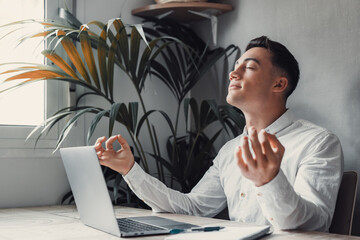 Serene office male employee sit at desk relaxing doing yoga, practice meditation to reduce stress...