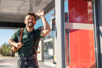 A happy man is stopping a bus on a city street.