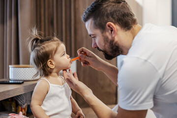 A father is giving a syrup and medicine to his baby girl. - obrazy, fototapety, plakaty
