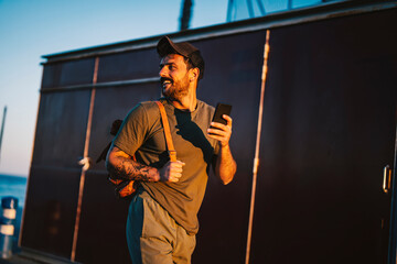 A happy casual man walking on the dock with his phone.