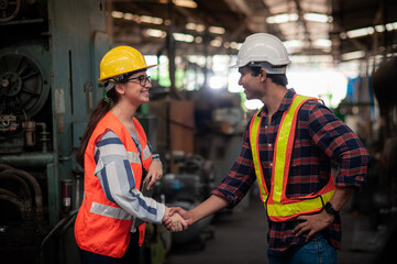 A smiling female engineer shakes hands to greet a tall, handsome, dark-skinned engineer wearing safety uniform workwear while working in an industrial factory.Teamwork and gender diversity concept.