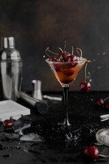 Refreshing alcoholic cocktail with cherries and ice in an elegant glass. Splashes from a summer fruit drink and melting ice on the table. 
