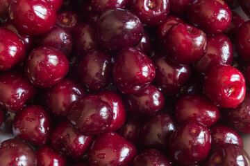 An extreme close-up of a bunch of fresh washed cherries in an overhead view, showing their details and textures. The cherries are bright red and glossy, with water drops on them.Food, fruit and summer