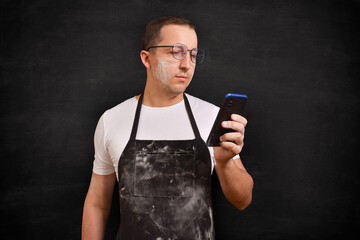 Male cook using a phone on a black background. The concept of cooking