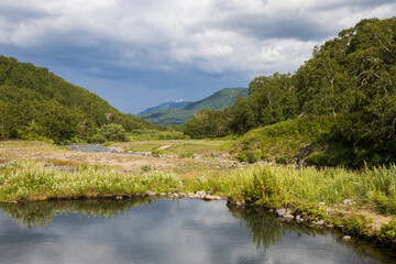 Fototapeta na wymiar Summer mountain landscape. View of the mountain valley. In the foreground is a lake with water from hot geothermal springs. Travel, tourism and hiking on the Kamchatka Peninsula. Far East of Russia.