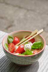 Healthy summer salad on a bowl with orange and red tomato, basil and goat cheese. Image with selective focus and copy space.