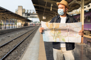 Man traveler backpack holding a map at the railway. Backpacker Asian adventure explore nature by train. Young male going to traveling by train. The concept of a man traveling alone.