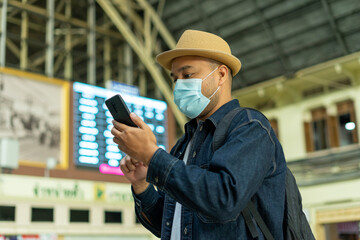Traveler male at train station check-in on smartphone  railway platform. Asian man with timetables information of departures arrivals on behind. Tourist adventure holiday traveling concept.