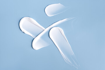 White smudges swatches smear of face or body care cream on a blue background
