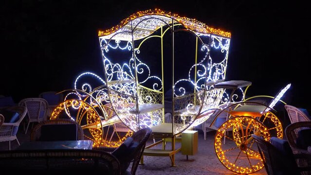An old carriage in garlands shines at night. Decoration in the form of a carriage with light bulbs on the summer terrace in a cafe.