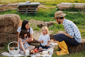 Happy young family having lunch at summer garden party. Mother, father and two kids enjoy spending time together on weekend at the countryside. Picnic with organic home-grown food. Healthy lifestyle.