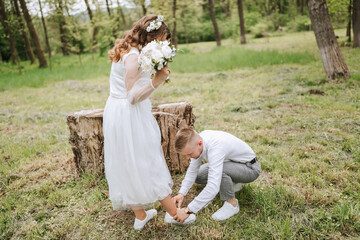 bridal walk in the forest. The groom is dressed in a white shirt and gray pants, helping the bride to tie her shoelaces