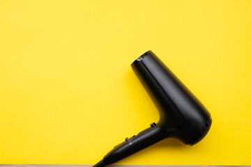 Black hair dryer on blue and yellow paper background.