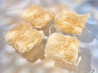 Rice noodles for Pad Thai, uncooked (raw), on blue background, dramatic lighting with strong shadows.