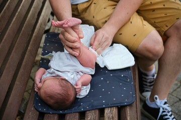 Young father changing the diaper to his newborn baby in a park. Four days old infant, parenthood concept. - obrazy, fototapety, plakaty