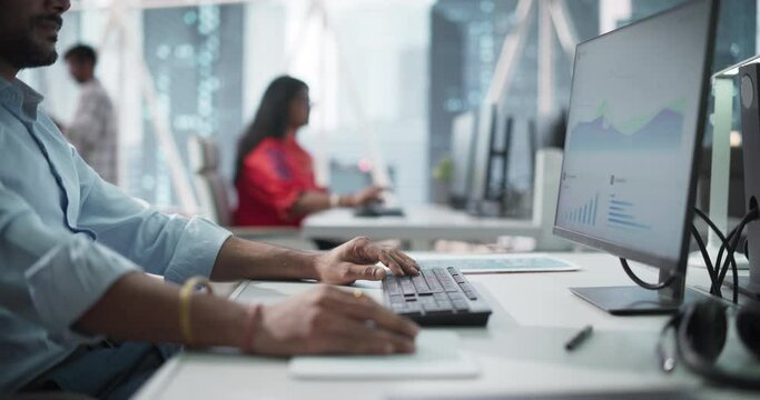 Close Up of a Young Indian Male Professional Working in a Business Research and Development Company. Handsome Manager Analyzing Financial Reports, Looking at a Computer Screen with Graphs and Charts