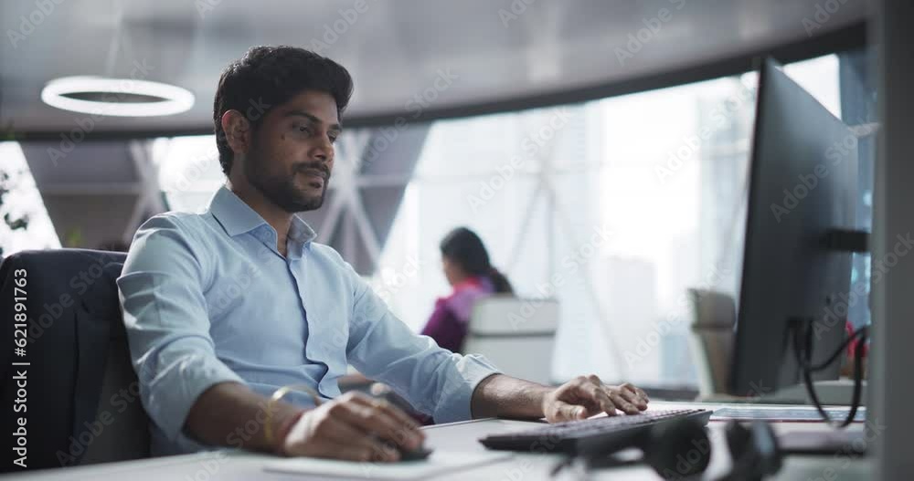Poster Portrait of a South Asian Financial Securities Trader Working on Desktop Computer in a Modern Office. Handsome Indian Accountant Bookkeeping Financial Affairs of a Business Venture
