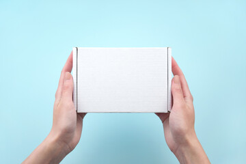 Female hands holding white package box on blue background.