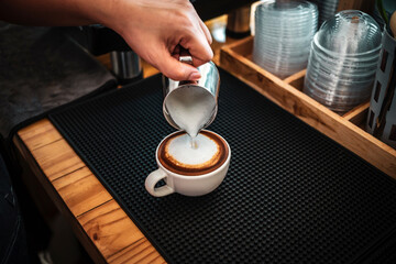 Barista hand pouring milk into coffee making a cappuccino. Professional barista preparing coffee on the counter.