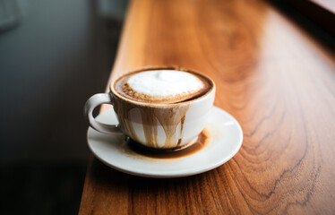 Spilled coffee with milk in a white cup or cappuccino is overflowing from the coffee cup on wooden bar