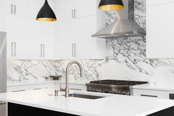 A kitchen detail with white cabinets, modern light fixtures hanging over a black island, and a...