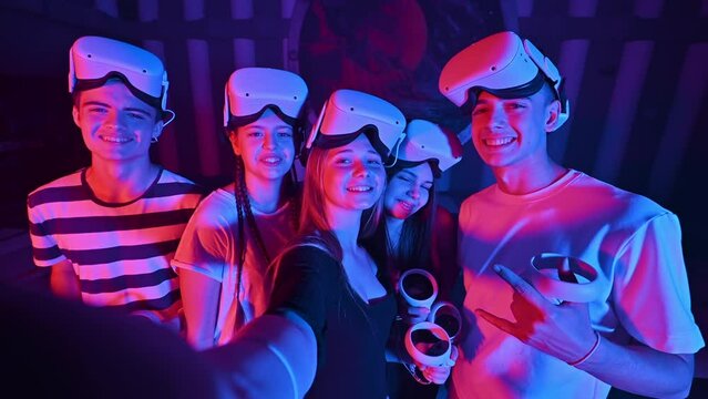 A team of young friends taking selfie while using virtual reality VR equipment on an arena. Neon lights