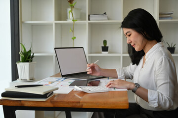 Portrait with Businesswoman, Accountant analyzing graphs, diagrams and figures in financial documents while working on laptop and digital tablet.