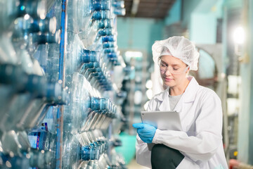 Female worker inspecting water bottle on production line in spring water factory