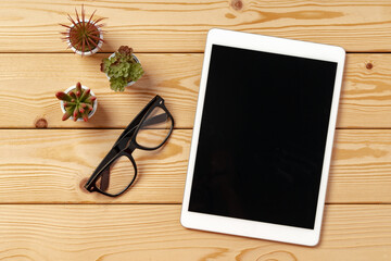 Top view of wooden table with white digital tablet with black screen on it