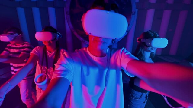 A team of young friends play virtual reality games in VR equipment on an arena. Neon lights