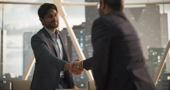 Young Indian Businesspeople Closing a Business Deal at a Meeting Room in Corporate Modern Office. Two Men in Classic Suits Shake Hands and Celebrate Successful Partnership