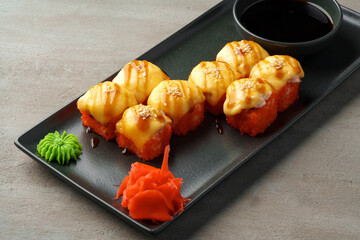 Baked sushi rolls on black plate on gray background