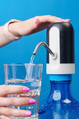 Woman's hands pouring water into a glass from water cooler on blue background