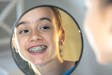 Caucasian preteen girl with braces on her teeth looking at the mirror.