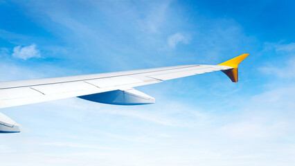 Airplane wing flying across the blue sky, window seat perespective, aerial background for travel operators and tourism promotion